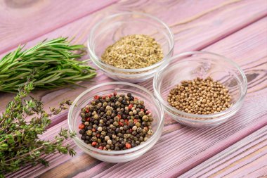 Mor ahşap arka planda cam kaselerde çeşitli baharatlar. Siyah ve kırmızı biber, kekik, kişniş.