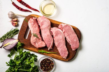 Kesme tahtasında çiğ et. Beyaz arka plan. Domuz eti pişirme hazırlığı. Yakınlarda çeşitli baharatlar ve baharatlar var..