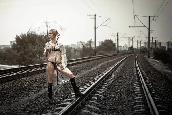 一个穿着透明雨衣 铁轨上挂着雨伞的女人 — 图库照片
