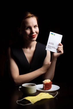 Kyiv, Ukrayna - 10 Kasım 2021: Bir kadın çay ve pastayla bir masada oturuyor ve uluslararası bir Ukrayna aşı sertifikası taşıyor.