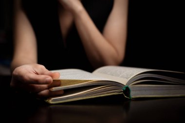 Karanlıkta kitap okuyan bir kadın. Masanın yanında oturuyor..