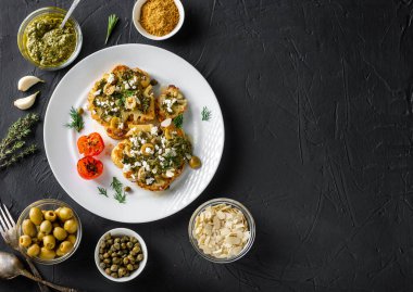 Baharatlı karnabahar bifteği, chimichurri sosu, badem gevreği, zeytin, kızarmış vişneli domates ve beyaz tabakta kapari. Karanlık arka plan. Kopyalama alanı.