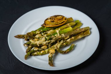 Beyaz tabakta peynir ve limonla pişirilmiş kuşkonmaz. Karanlık arka plan. Vejetaryen yemeği. Sağlıklı yemek..