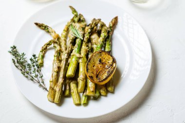 Peynirli kuşkonmaz, otlar ve limonlu baharatlar beyaz tabakta. Beyaz arka plan. Vejetaryen yemeği. Sağlıklı yemek..