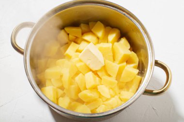 Tencerede haşlanmış patates. Bir parça tereyağlı sıcak patates küpleri. Haşlanmış patates, patates püresi. Buhar geliyor. Beyaz arkaplan.