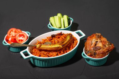 Kızarmış muzlu jollof pilav, fırında tavuk. Domatesli pilav, soğan, baharat. Geleneksel Nijerya yemekleri. Koyu arkaplan.