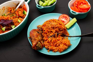 Tavuklu jollof pilavı tabakta. Domatesli pilav, soğan, baharat. Geleneksel Nijerya yemekleri. Koyu arkaplan.
