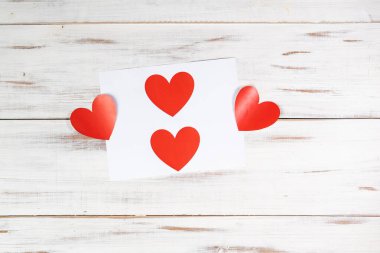 Beyaz ahşap arka planda kağıda basılmış kırmızı kağıt kalpler. Aşk Bildirgesi, Sevgililer Günü Konsepti.