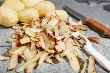 Çiğ patates soymak. Masasında bıçak olan bir sürü patates kabuğu. Yemek hazırlığı.
