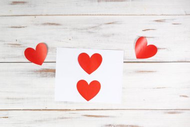 Beyaz ahşap arka planda kağıda basılmış kırmızı kağıt kalpler. Aşk Bildirgesi, Sevgililer Günü Konsepti.