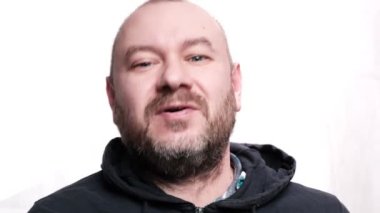 Adam kameraya kibarca konuşuyor. Beyaz arka plan. Orta yaşlı bir adam, kırk yaşında. Tıraşsız adam.