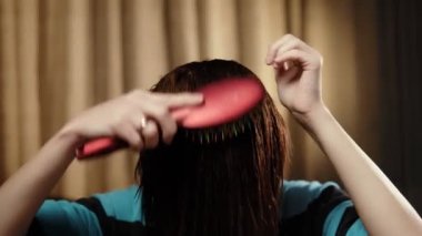 Tanınmayan bir kadın ıslak saçlarını bir tarakla tarıyor. Yakın plan. Saç bakımı. Koyu arkaplan.