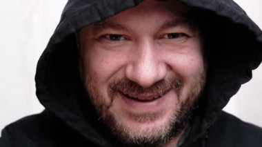 Adam kameraya bakarak güler. Sakallı, orta yaşlı bir adam. Başında bir kapüşon. Beyaz arka plan. Yakın plan..