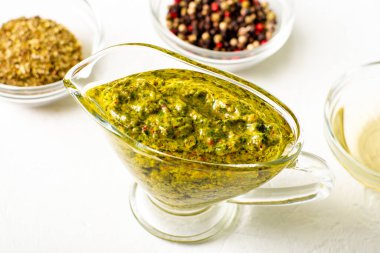 Beyaz arka planda soslu Chimichurri sosu. Yakınlarda çeşitli baharatlar var. Arjantin vejetaryen sosu zeytinyağı, kekik, maydanoz.