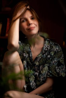 Kadın bitkilerin içinde evde dinleniyor. 40 yaşında çekici bir kadın. Evde dinlenme, dinlenme..