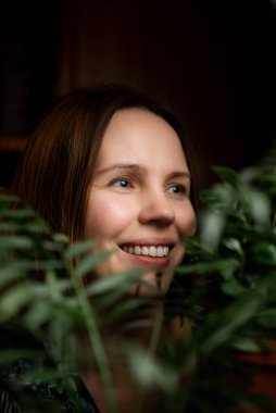 Yeşil bitkiler içinde gülümseyen orta yaşlı bir kadının portresi. Kırklı yaşlarda bir kadın. Rahatlama, sakinleşme, mutlu yüz..