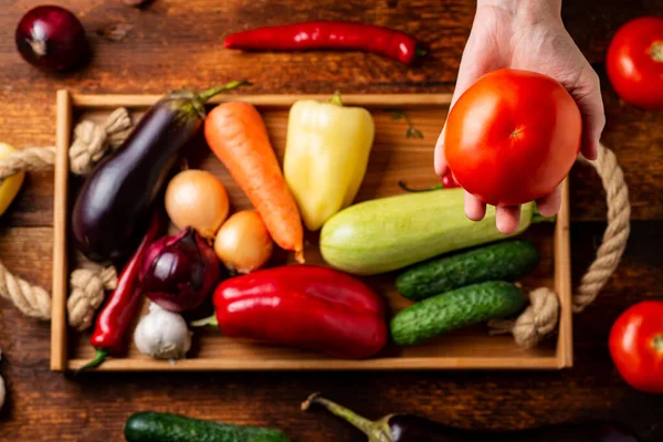 Tanınmayan bir kadın elinde farklı sebzelerin arka planında domates tutuyor. Sağlıklı gıda ve vejetaryenlik kavramı.