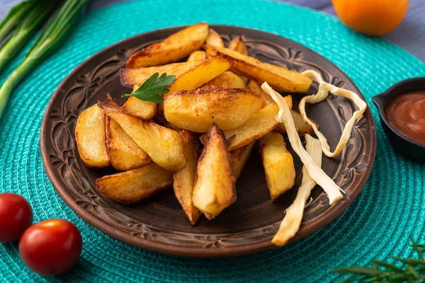 Tabakta büyük parçalar halinde patates kızartması. Masada turkuaz peçete ve farklı sebzeler var..