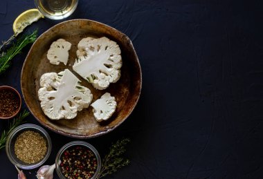 Karnabahar bifteği, yemek tarifi. Karnabahar 'ın çiğ parçaları kızartma tavasında yatıyor. Zeytinyağının yanında, baharatlar. Karanlık arka plan. Metin için yer.