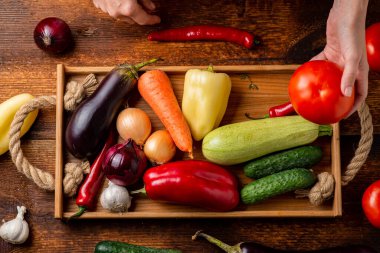 Tanınmayan bir kadın elinde farklı sebzelerin arka planında domates tutuyor. Sağlıklı gıda ve vejetaryenlik kavramı.