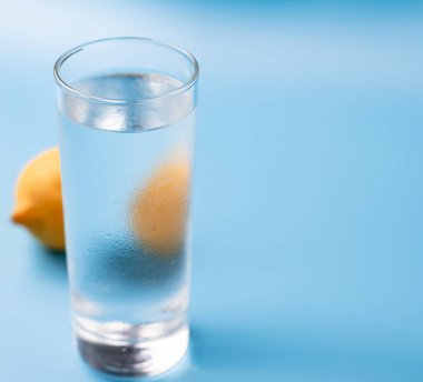 Mavi arka planda limonlu bir bardak saf soğuk su.