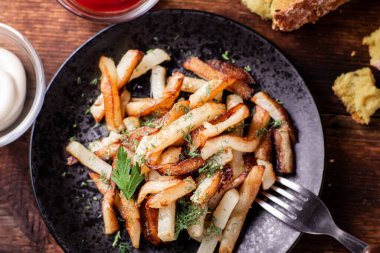 Ketçaplı kızarmış patates, mayonez ve ahşap arka planda otlar..