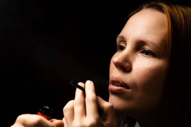 Kadın marihuana içiyor, esrarı siyah arka plandaki bir cihazdan geçiriyor..