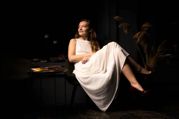 Молодая Женщина Белом Платье Сидит Расслабленно Кресле Темной Комнате — стоковое фото