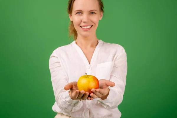 40歳の美しい女性が緑の背景に手に新鮮なリンゴを持っています 健康的な食事 菜食主義 健康的な外観の概念 — ストック写真