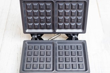 Beyaz ahşap arka planda elektrikli waffle ızgarası. Belçika waffle 'ı yapmak için aygıt.