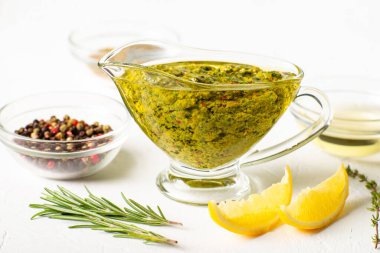 Beyaz arka planda soslu Chimichurri sosu. Yakınlarda çeşitli baharatlar var. Arjantin vejetaryen sosu zeytinyağı, kekik, maydanoz.