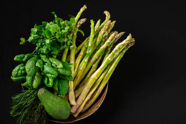 Various green vegetables on a dark background. Asparagus, spinach, avocado. Vegetarian food concept. Place for text. Top view.