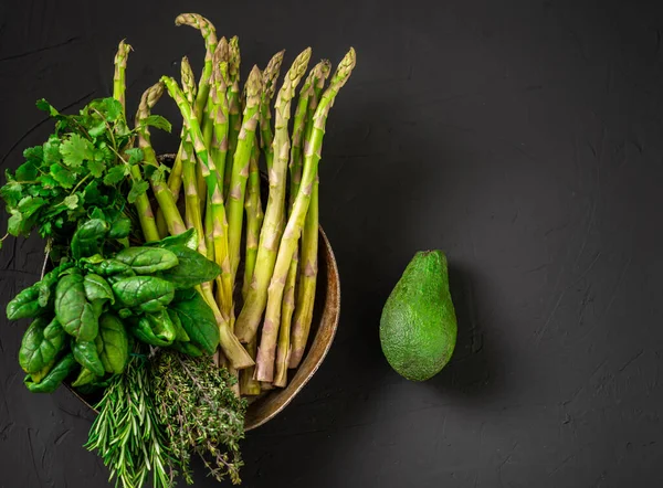 Avocado and various green vegetables on a dark background. Asparagus, spinach, rosemary. Vegetarian food concept.