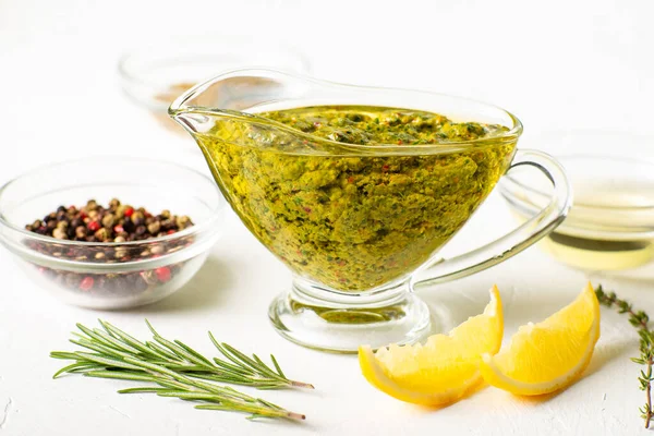 Beyaz arka planda soslu Chimichurri sosu. Yakınlarda çeşitli baharatlar var. Arjantin vejetaryen sosu zeytinyağı, kekik, maydanoz.