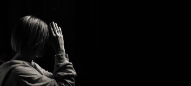 Woman praying with her head bowed with folded palms on a black background. Black and white painting. Banner.