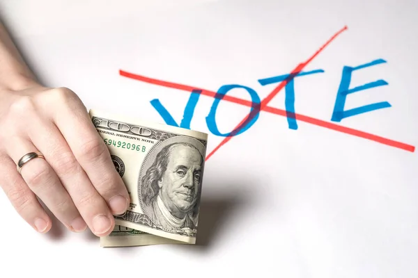 Buying votes of voters concept. A woman\'s hand holds one hundred US dollars against the background of the crossed out word vote.