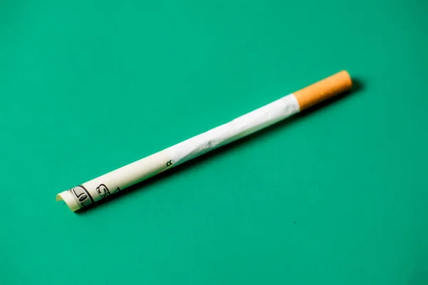 Smoking and money. Rolled up dollar bill in a cigarette. Green background. The high cost of smoking cigarettes concept.