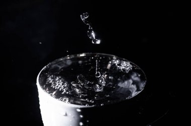 Siyah arkaplanda bir damla su damlası olan bir fincan..