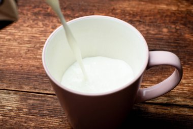 Süt kahverengi ahşap bir arka planda bir fincana dökülür..