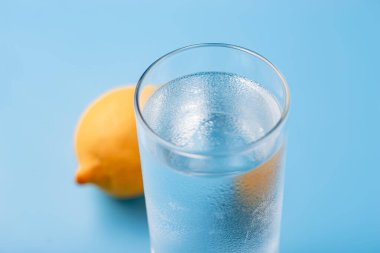 Mavi arka planda limonlu bir bardak saf soğuk su.