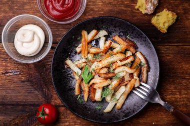 Tabakta patates kızartması ve ahşap bir arka planda otlar. Ketçap, mayonez ve ekmek yan yana..