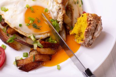 Yumurtalı kızarmış patates, sıvı sarısı, otlar ve domatesler beyaz tabakta..