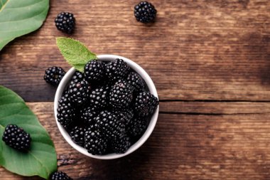 Taze böğürtlen böğürtlenleri ahşap bir arka planda beyaz bir kasede yakın planda.