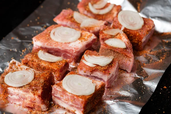 生の玉ねぎと豚の肋骨は オーブンで焼かれる準備ができて 箔に横たわっています — ストック写真
