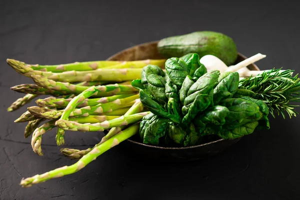 Various green vegetables on a dark background. Asparagus, spinach, avocado, garlic. Vegetarian food concept.