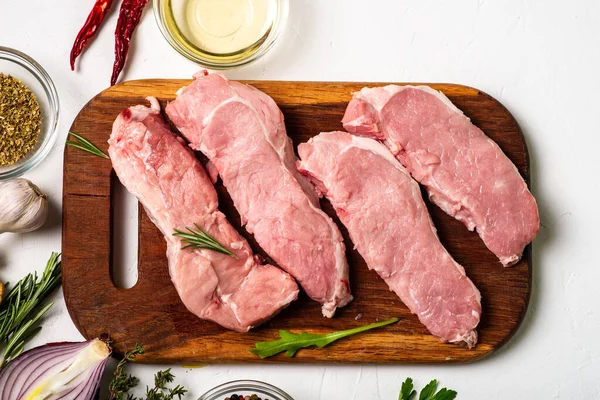 Kesme tahtasında çiğ et. Beyaz arka plan. Domuz eti pişirme hazırlığı. Yakınlarda çeşitli baharatlar ve baharatlar var..