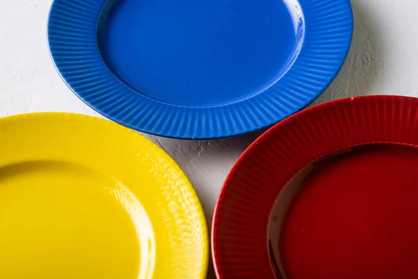 Different colors of empty plates. White background. Red, blue and yellow clay plate.