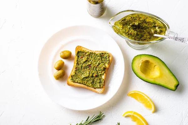 toast with avocado, olives and chimichurri sauce on a white plate. Healthy vegetarian food. White background.