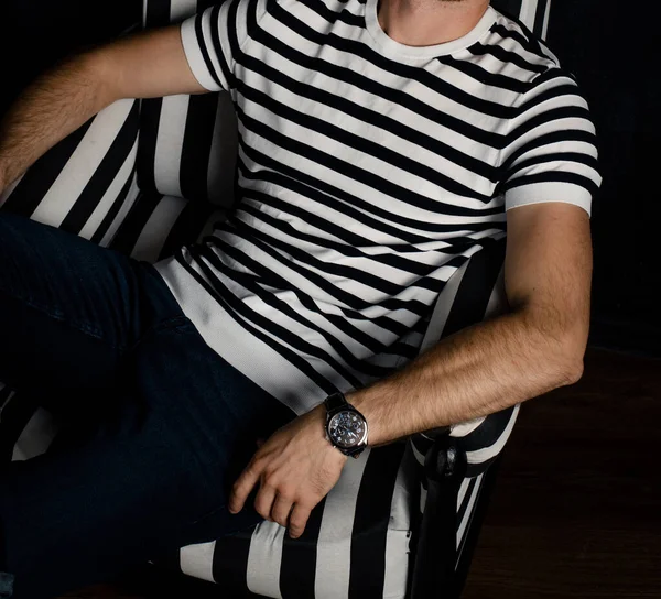 An unrecognizable man in a striped T-shirt sits on a striped armchair.