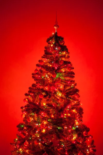 Χριστουγεννιάτικο δέντρο με φωτισμό, κόκκινο φόντο — Φωτογραφία Αρχείου